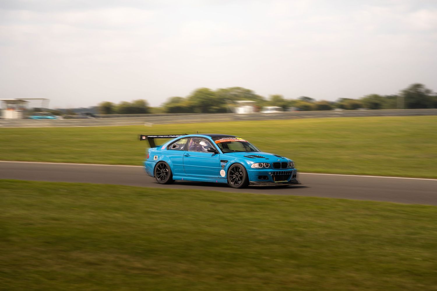 Blue BMW touring car racing on a green grass-lined circuit.