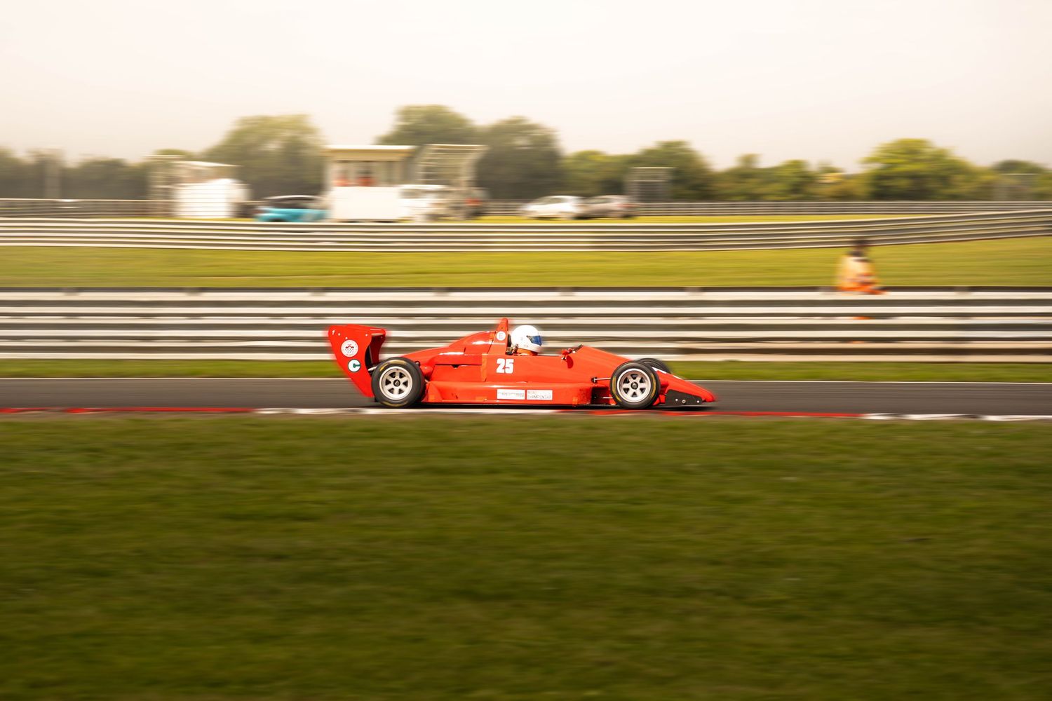 Red open-wheel formula racing car speeding along a motorsport circuit at sunset.