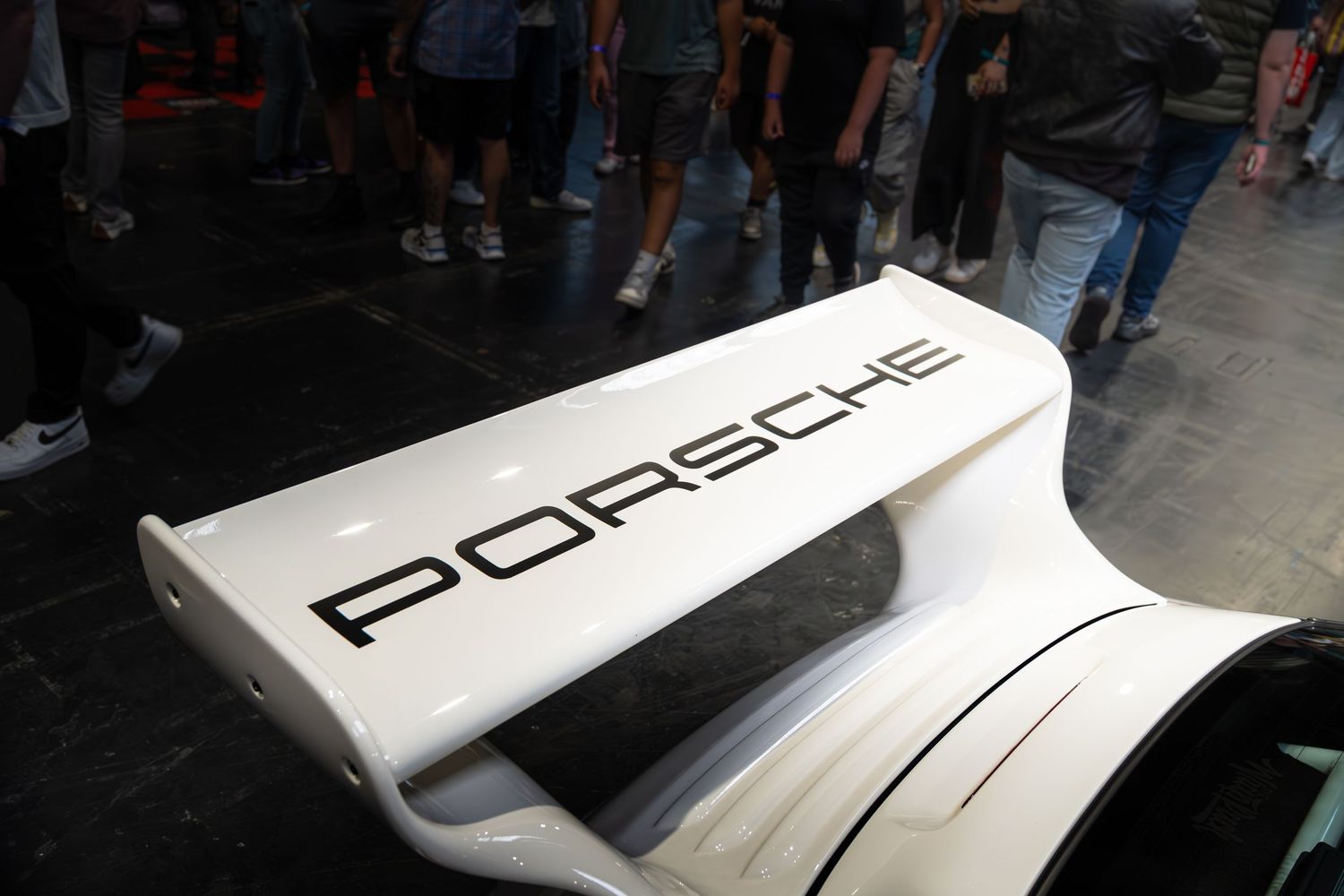 White Porsche rear spoiler wing with bold black Porsche lettering at motorsport event.