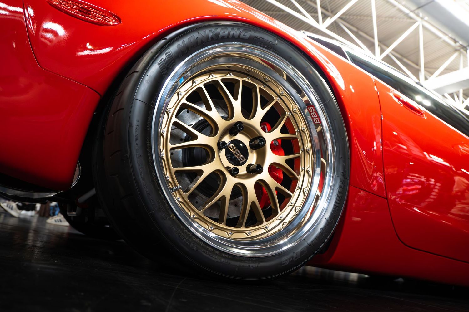 Close-up of a gold BBS wheel with red brake caliper on a red sports car.