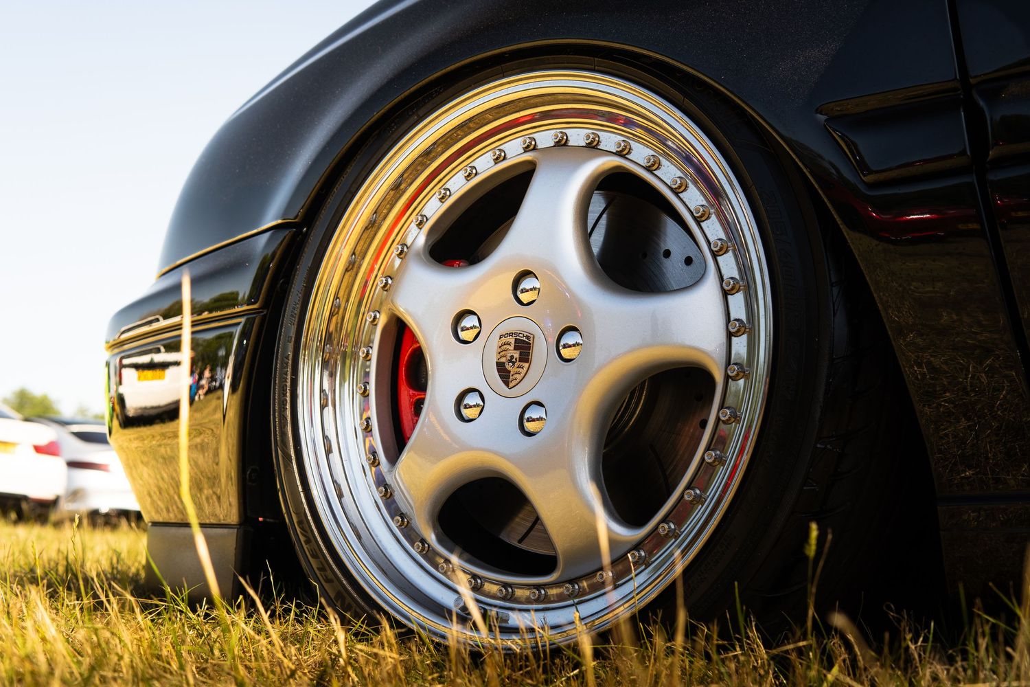 Classic Porsche three-piece split rim alloy wheel with red brake caliper on black car.