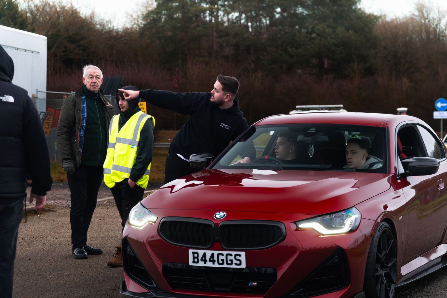 Marshals in hi-vis direct red BMW M2 supercar at UK track day event on overcast winter day.