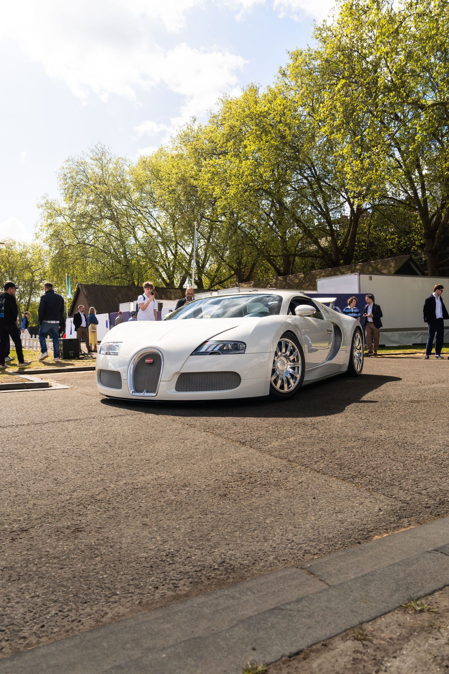 A white Bugatti Veyron supercar parked at an outdoor automotive event with trees in the background.