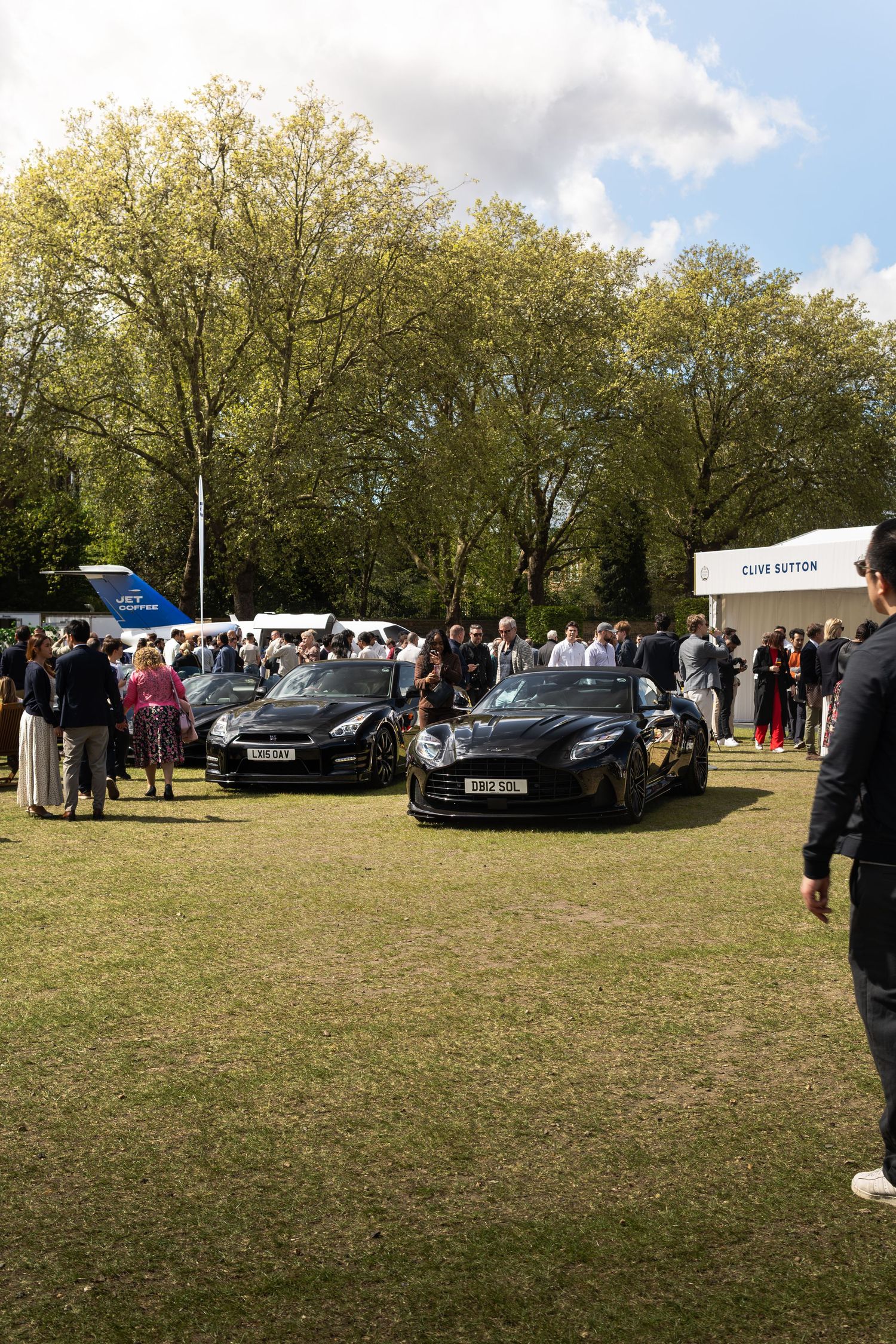 Black supercars on display at an outdoor automotive show with crowds of spectators on a sunny day.