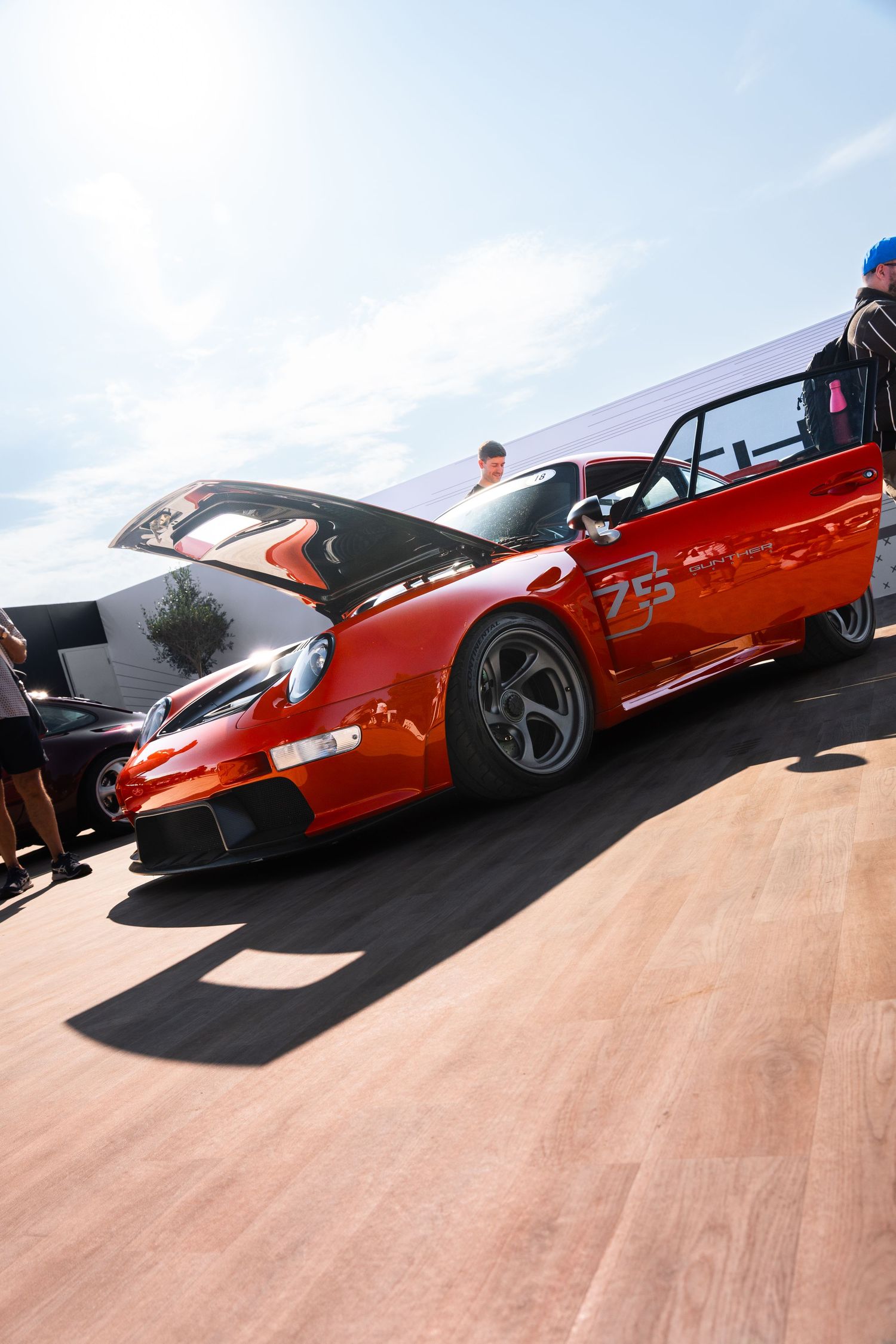 Red Porsche 911 race car number 25 with open hood at a motorsport event on a sunny day.