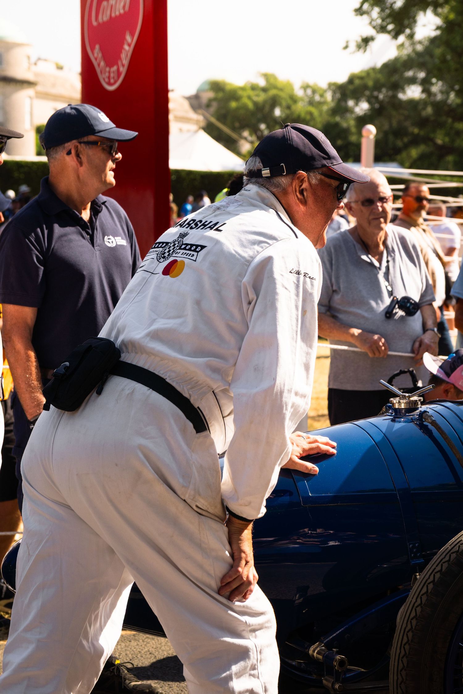 A marshal in white overalls inspects a vintage blue racing car at the Goodwood Festival of Speed event.