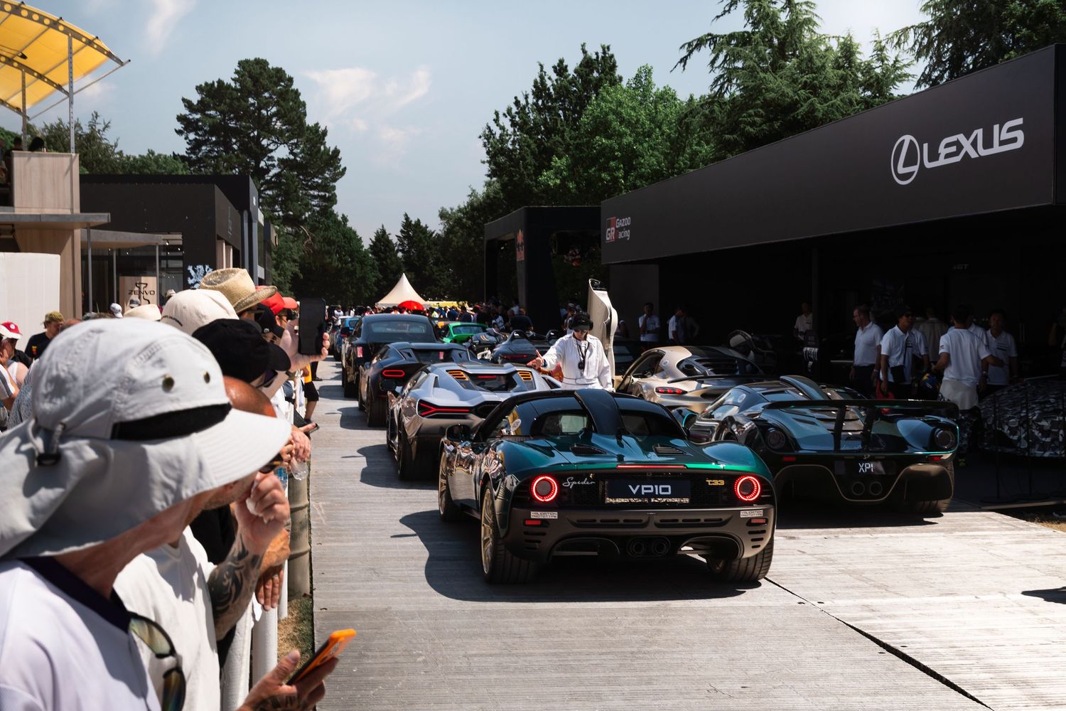 Luxury sports cars lined up at a Lexus automotive event with spectators watching from behind barriers.