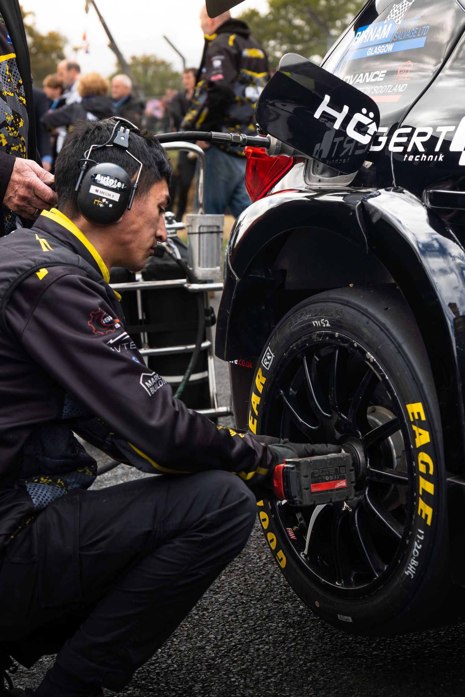 Mechanic using air gun to change tire on BTCC race car with Goodyear Eagle tires at circuit.