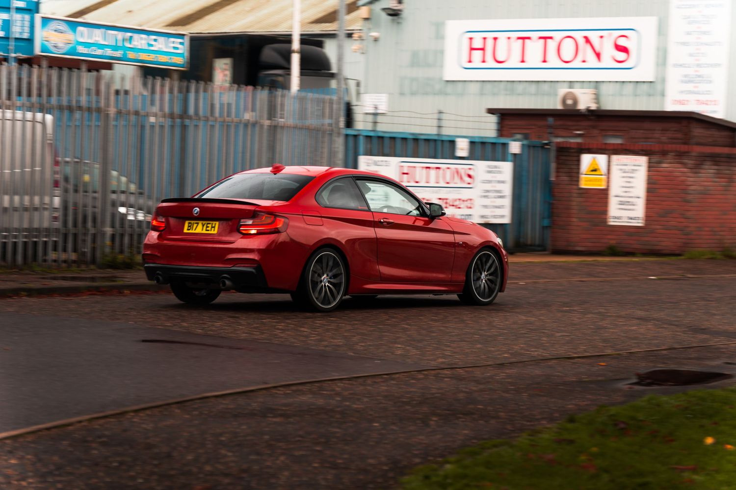 Red BMW M2 coupe parked outside Huttons industrial warehouse building.