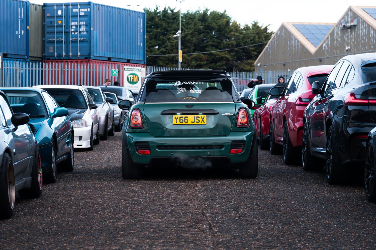 A green Mini Cooper parked between rows of cars at an outdoor automotive event.