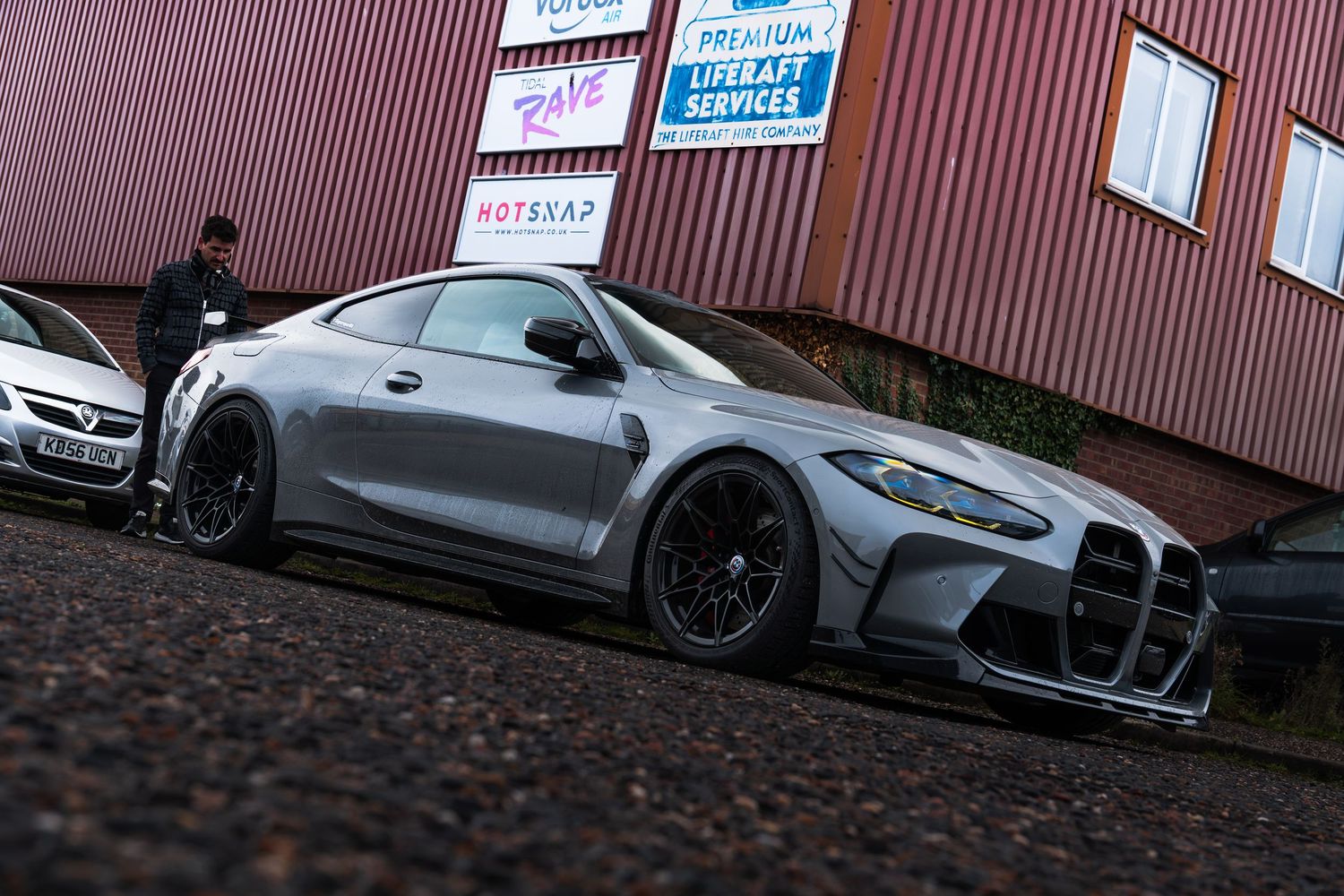 A wide-body grey BMW M4 with aggressive aero kit parked outside a Premium Supercar Services building.