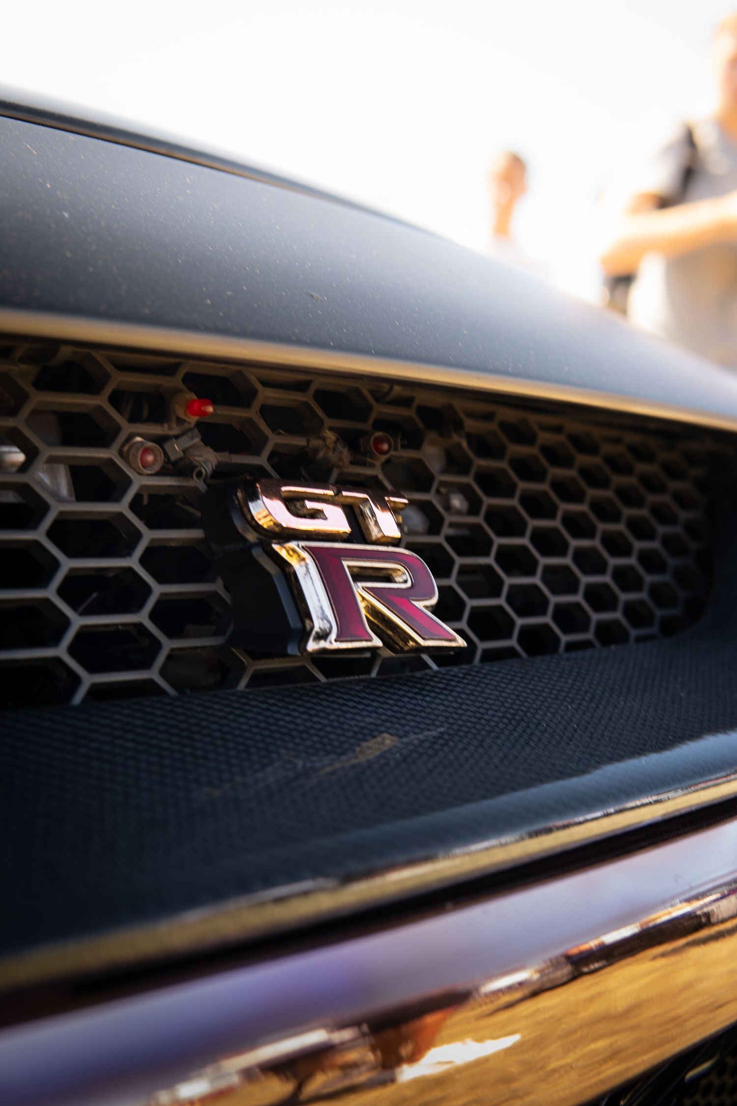 Close-up of Nissan GT-R chrome grille badge on dark honeycomb front grille.
