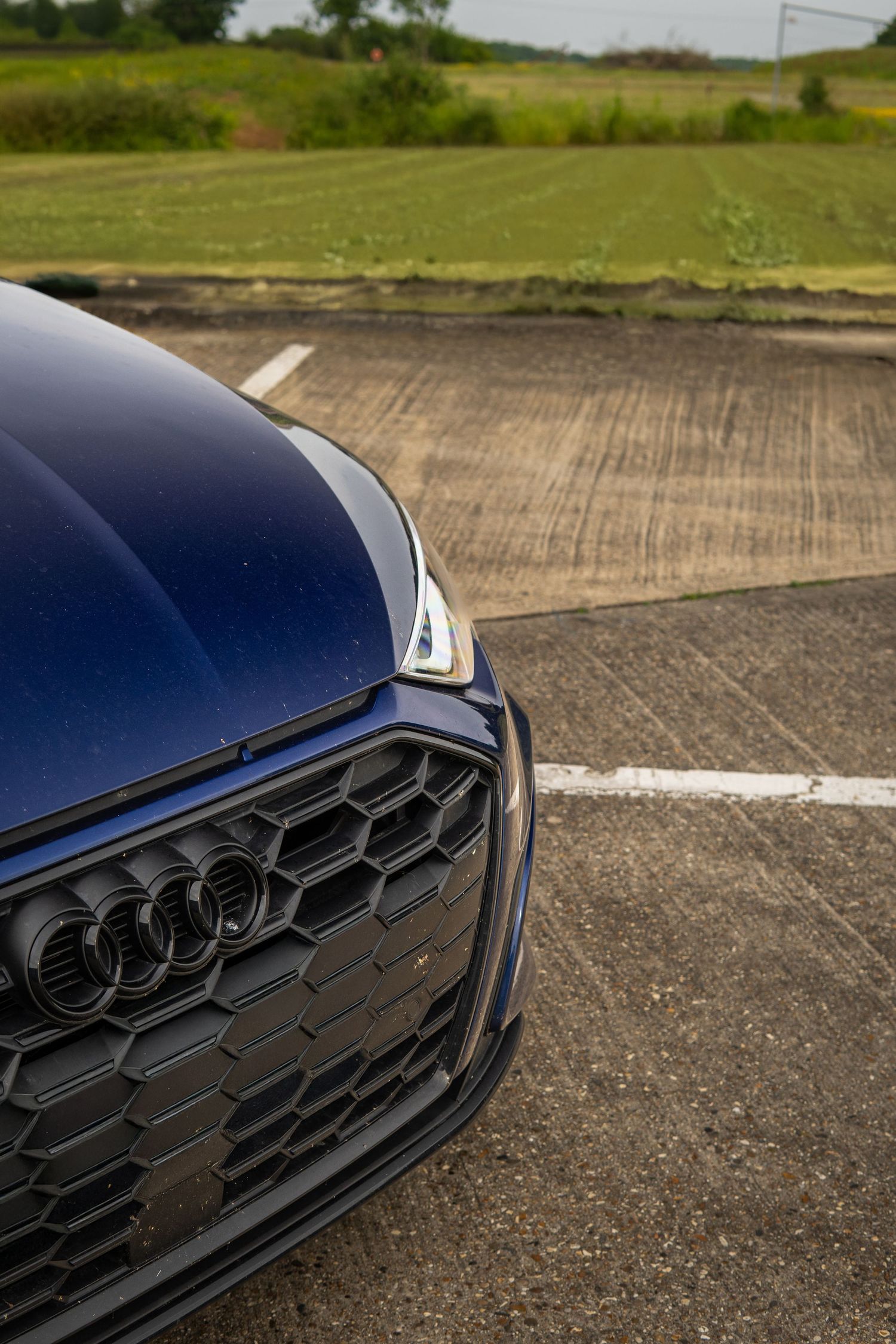Close-up of the navy blue Audi S3 front grille and hood badge in a parking area.