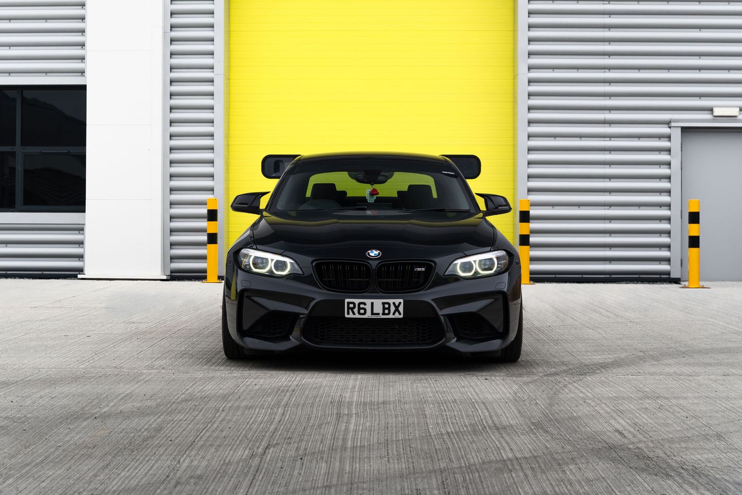 Black BMW M2 coupe front view parked in front of yellow garage doors.
