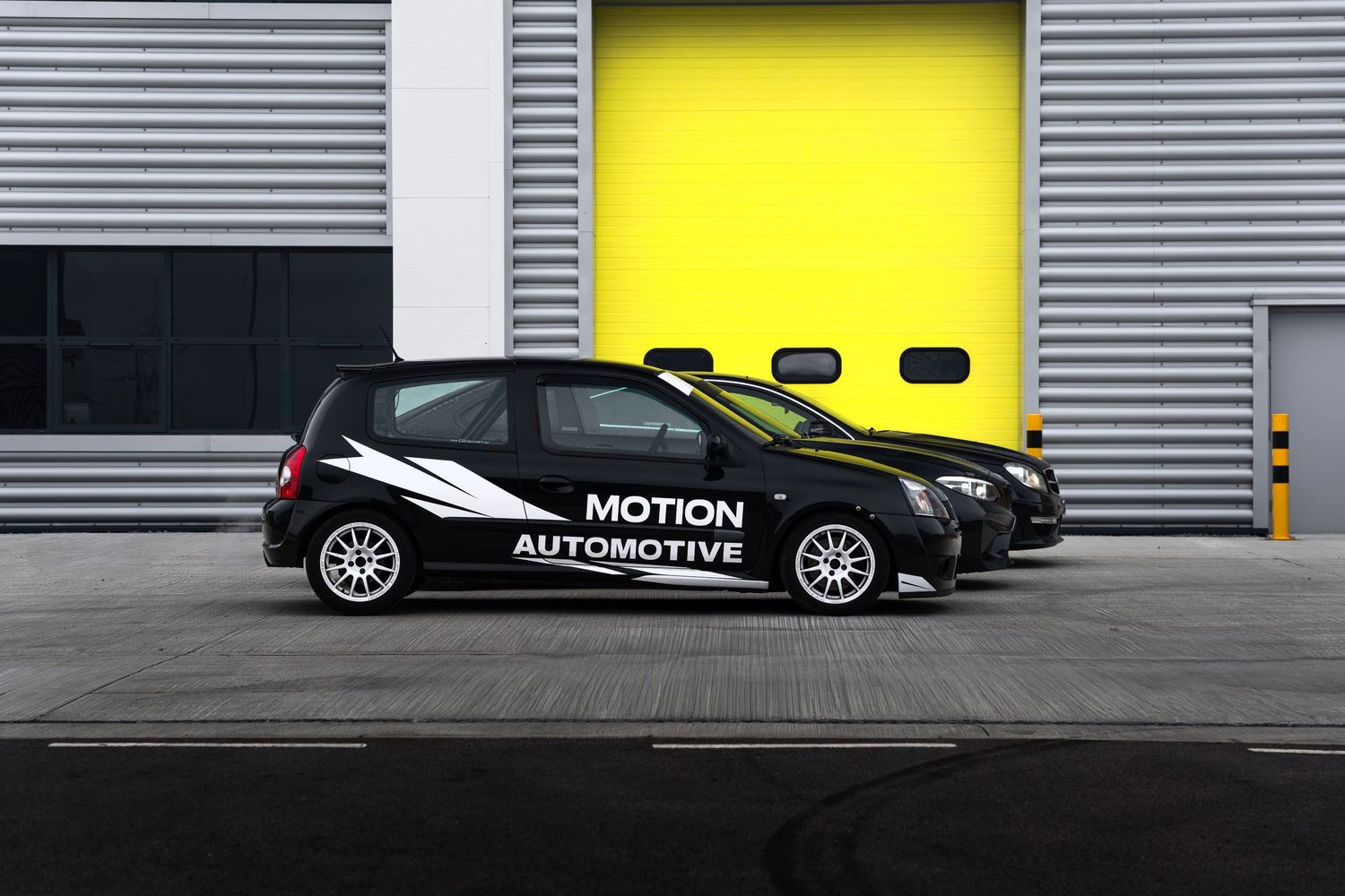 Side view of three black Motion Automotive cars parked outside a building with a yellow roller door.
