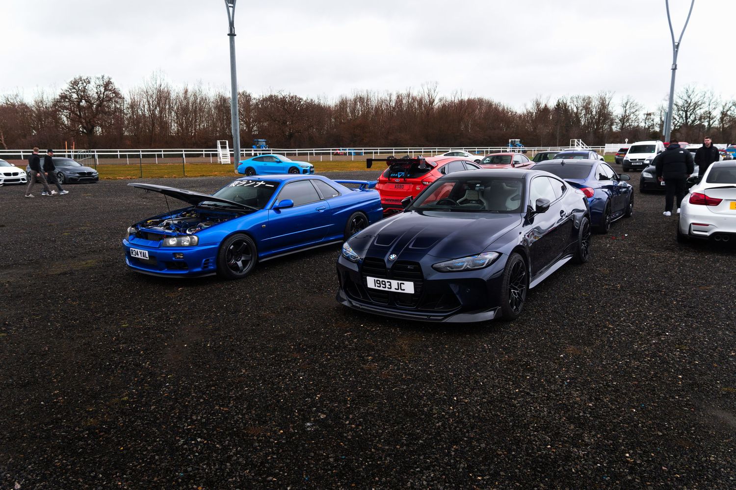 Blue Nissan Skyline and dark BMW parked at an outdoor automotive car show.
