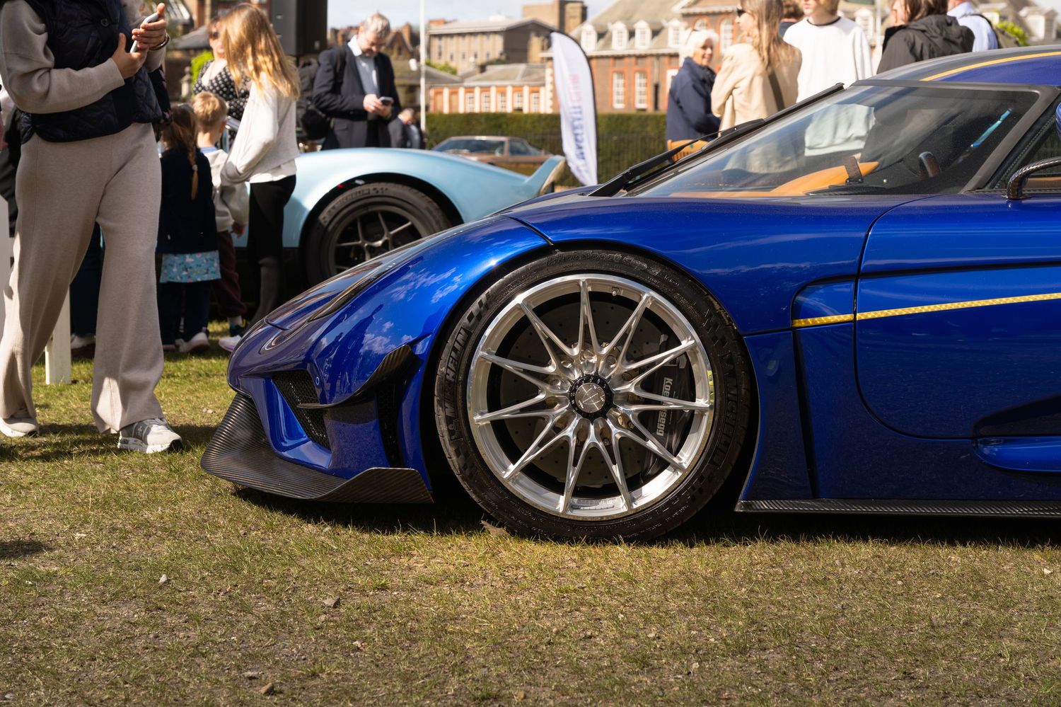Close-up of blue Koenigsegg Regera front wheel and carbon fiber bodywork at a car show.