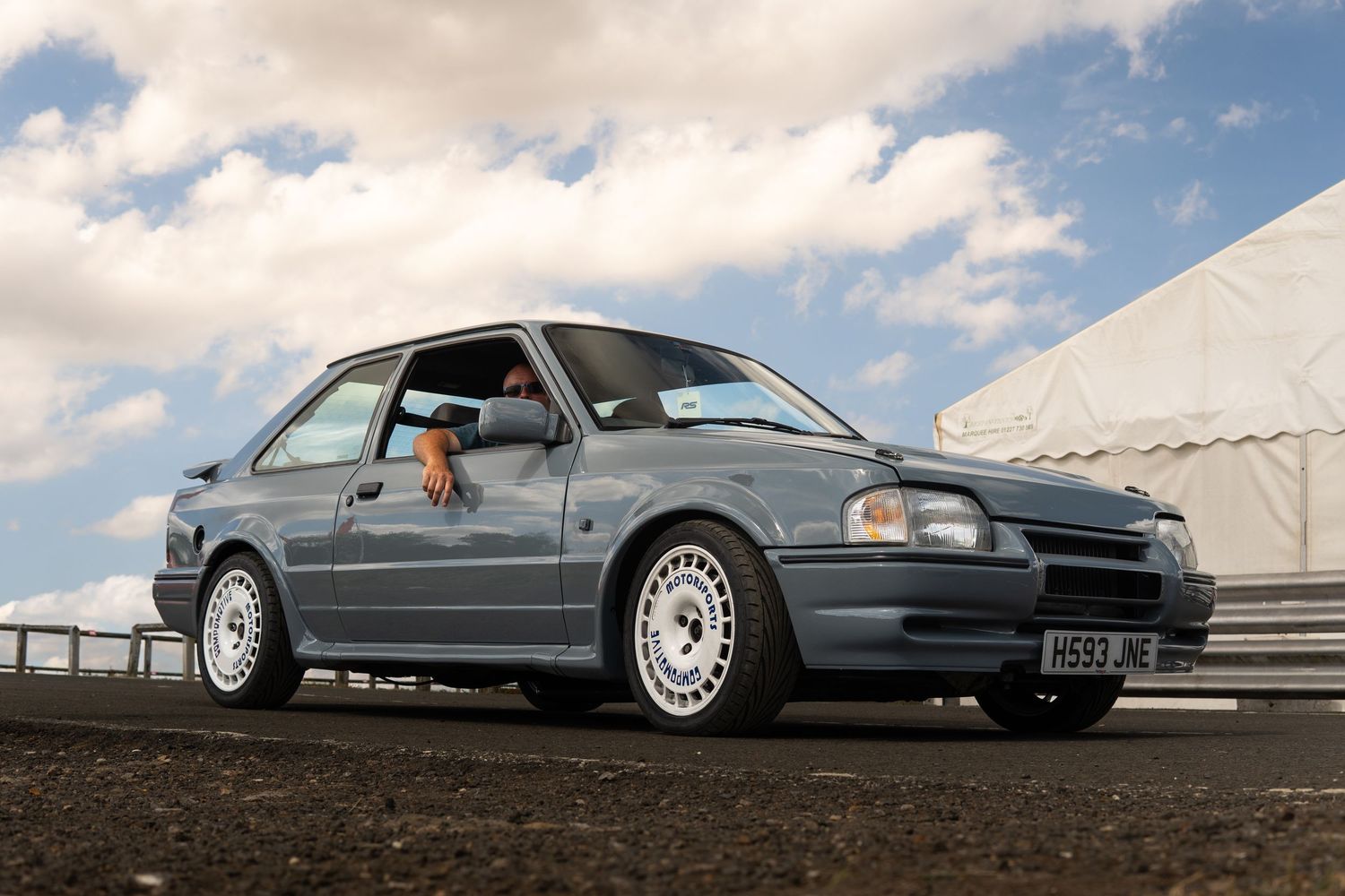Grey Vauxhall Astra GTE with white alloy wheels on a tarmac surface under cloudy skies.