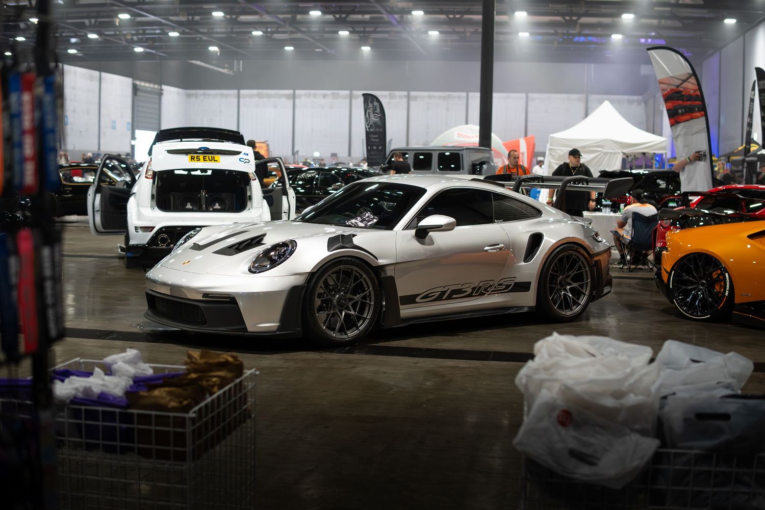 White Porsche 911 GT3 RS on display inside a large indoor car show hall.