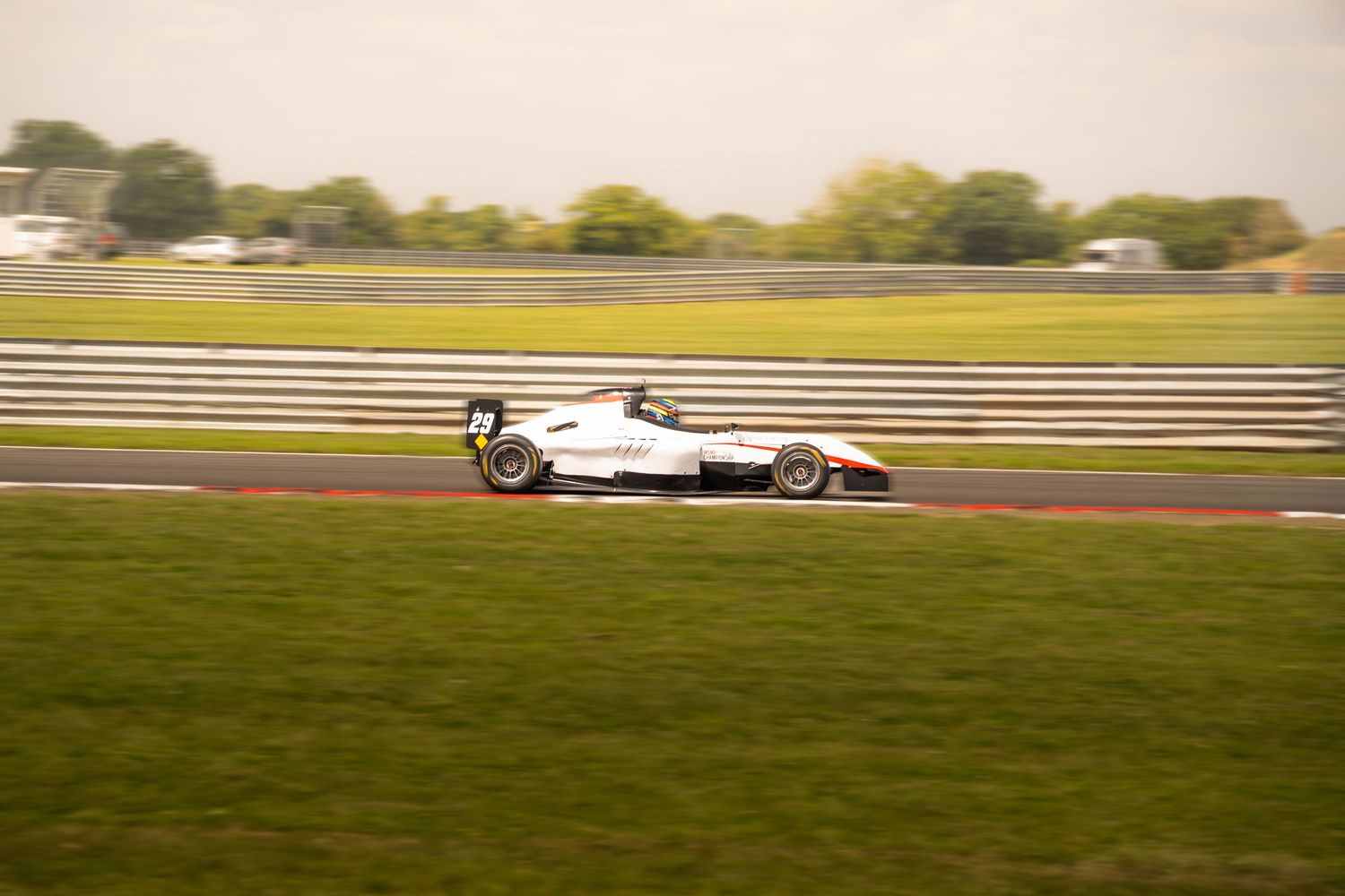 White open-wheel formula racing car speeding along a motorsport circuit track.