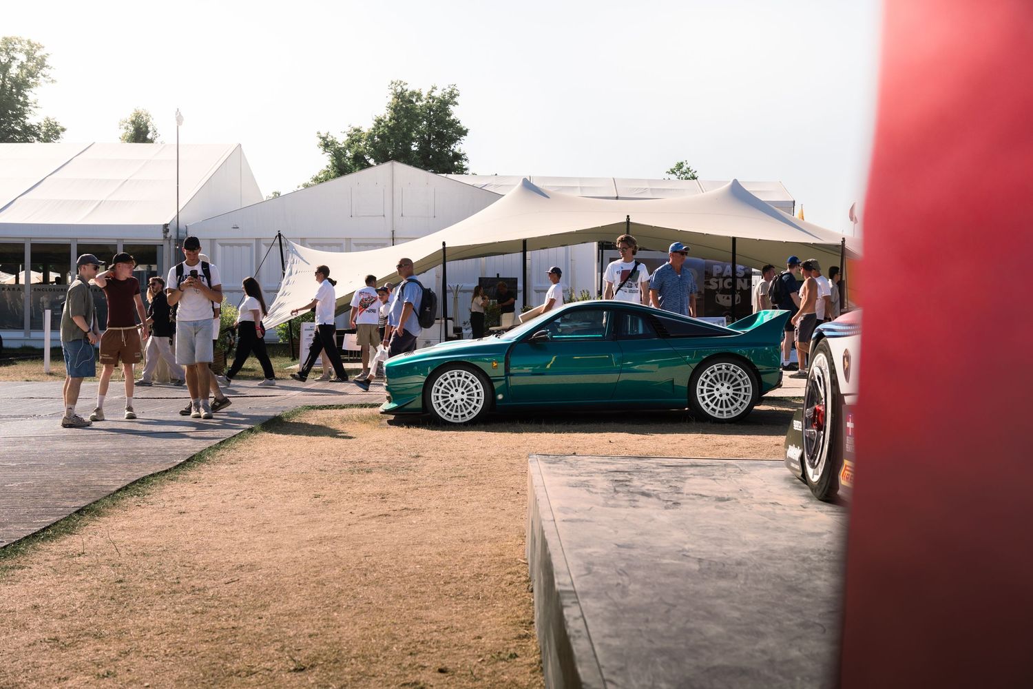 A green sports car on display at an outdoor car show with white tents and spectators in the background.