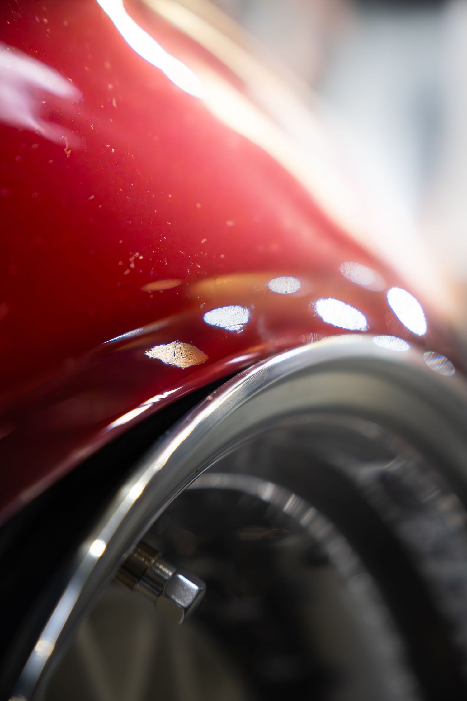 Macro shot of glossy red car bodywork with chrome wheel arch and reflective paint finish.