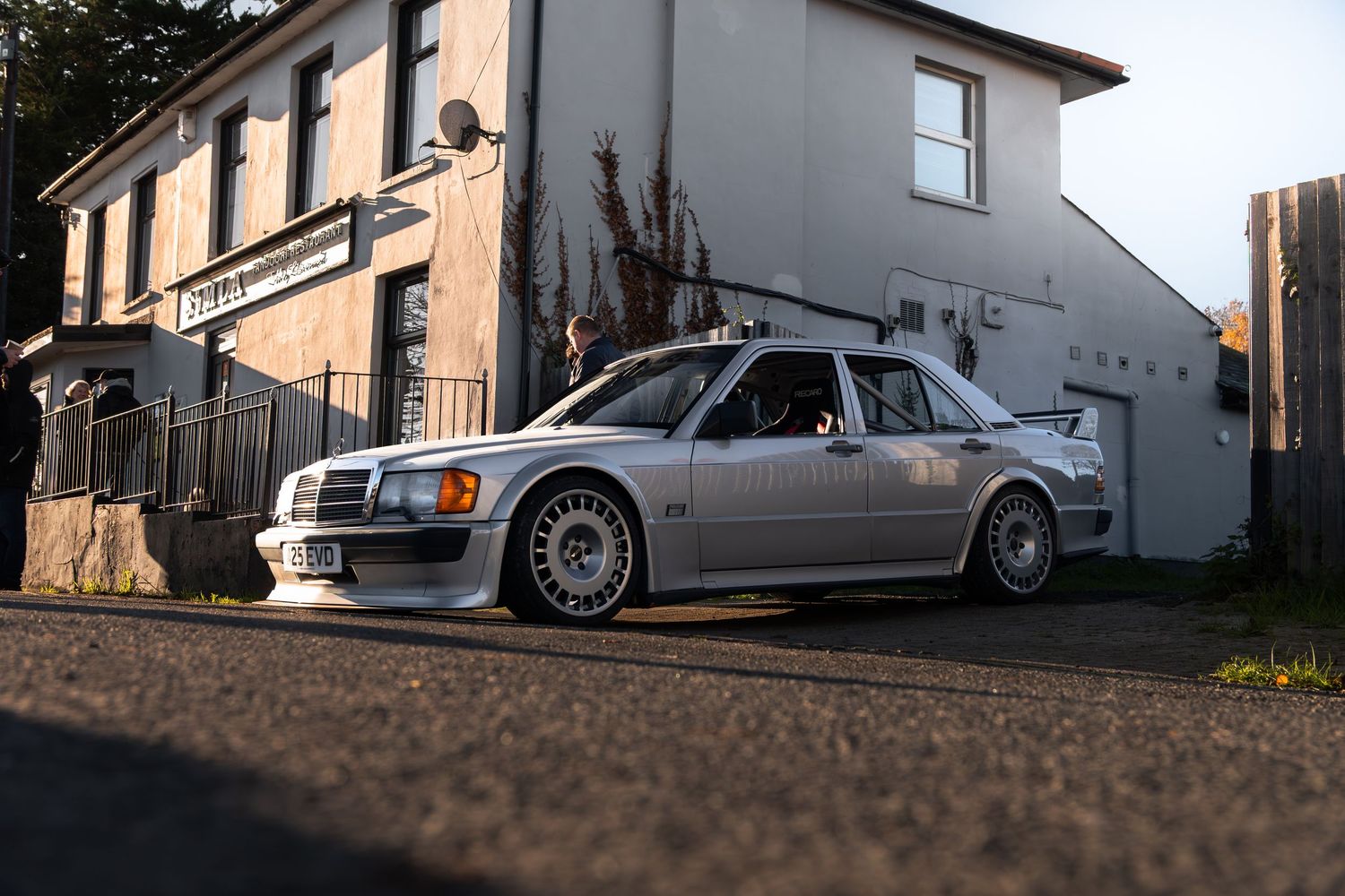 Silver Mercedes-Benz 190E Evolution wide body kit parked outside a building at golden hour.