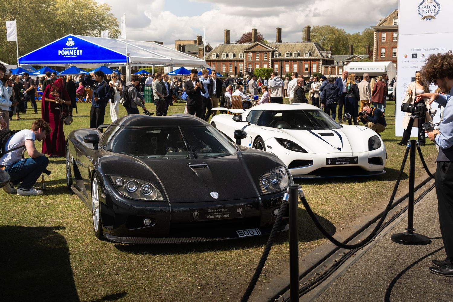 Black and white Koenigsegg supercars displayed at an outdoor car show near a historic building.