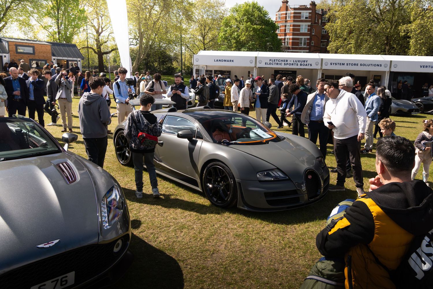 Matte grey Bugatti Veyron surrounded by crowds at an outdoor luxury car exhibition.