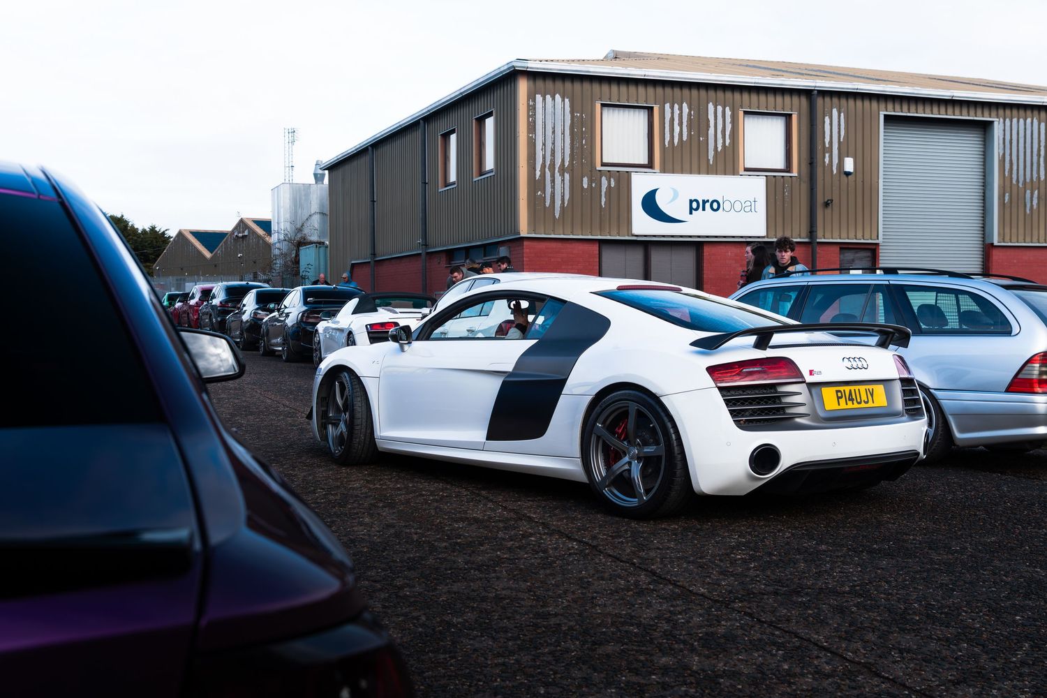 White Audi R8 parked outside a Pro Cars dealership building with other vehicles.