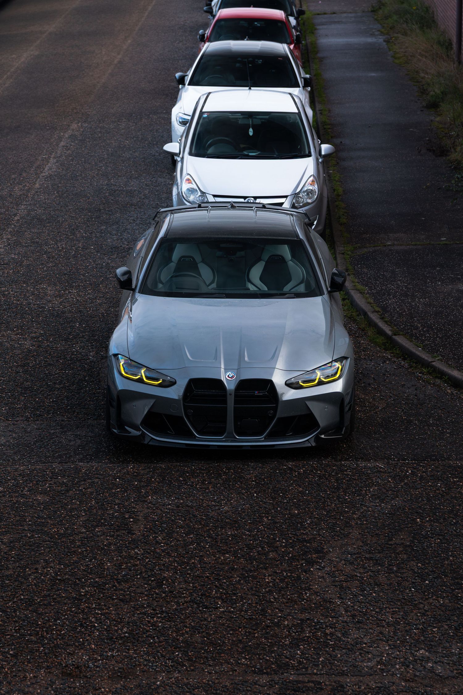 Top-down view of a silver BMW M3 G80 with yellow DRL headlights parked in a row.