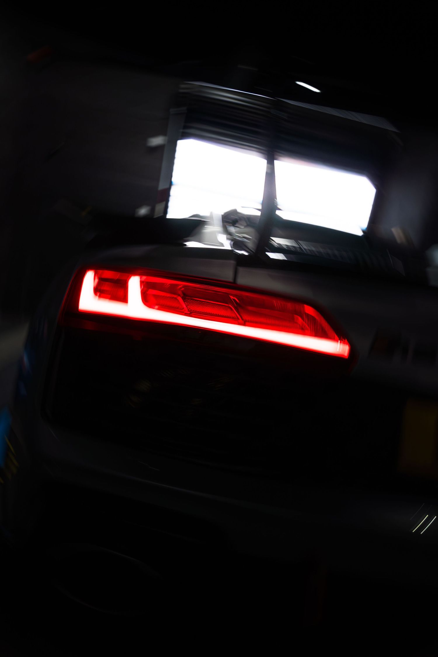 Dark moody shot of a red illuminated Audi R8 tail light inside a dimly lit garage.
