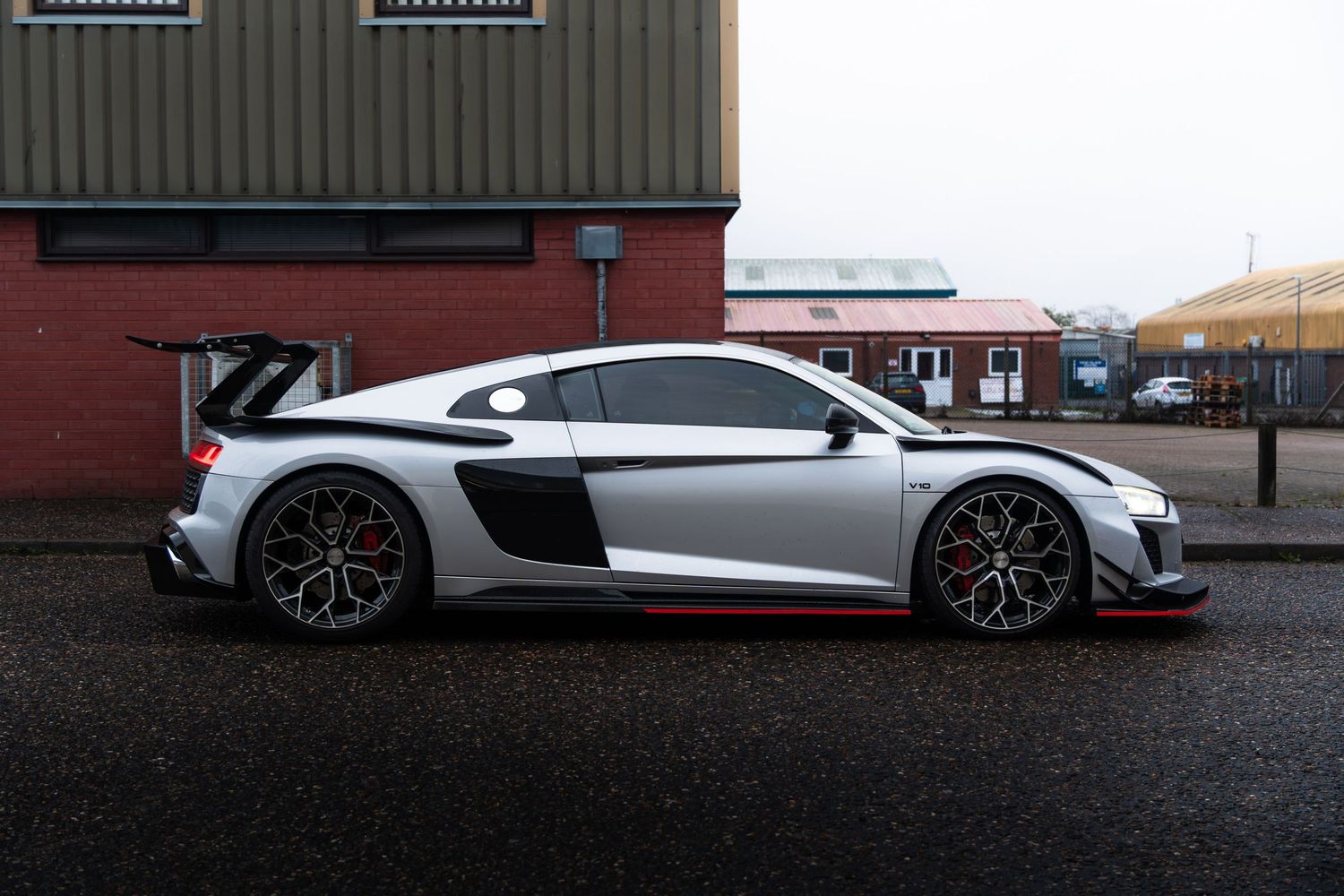 Silver Audi R8 GT3 race car parked beside an industrial building.