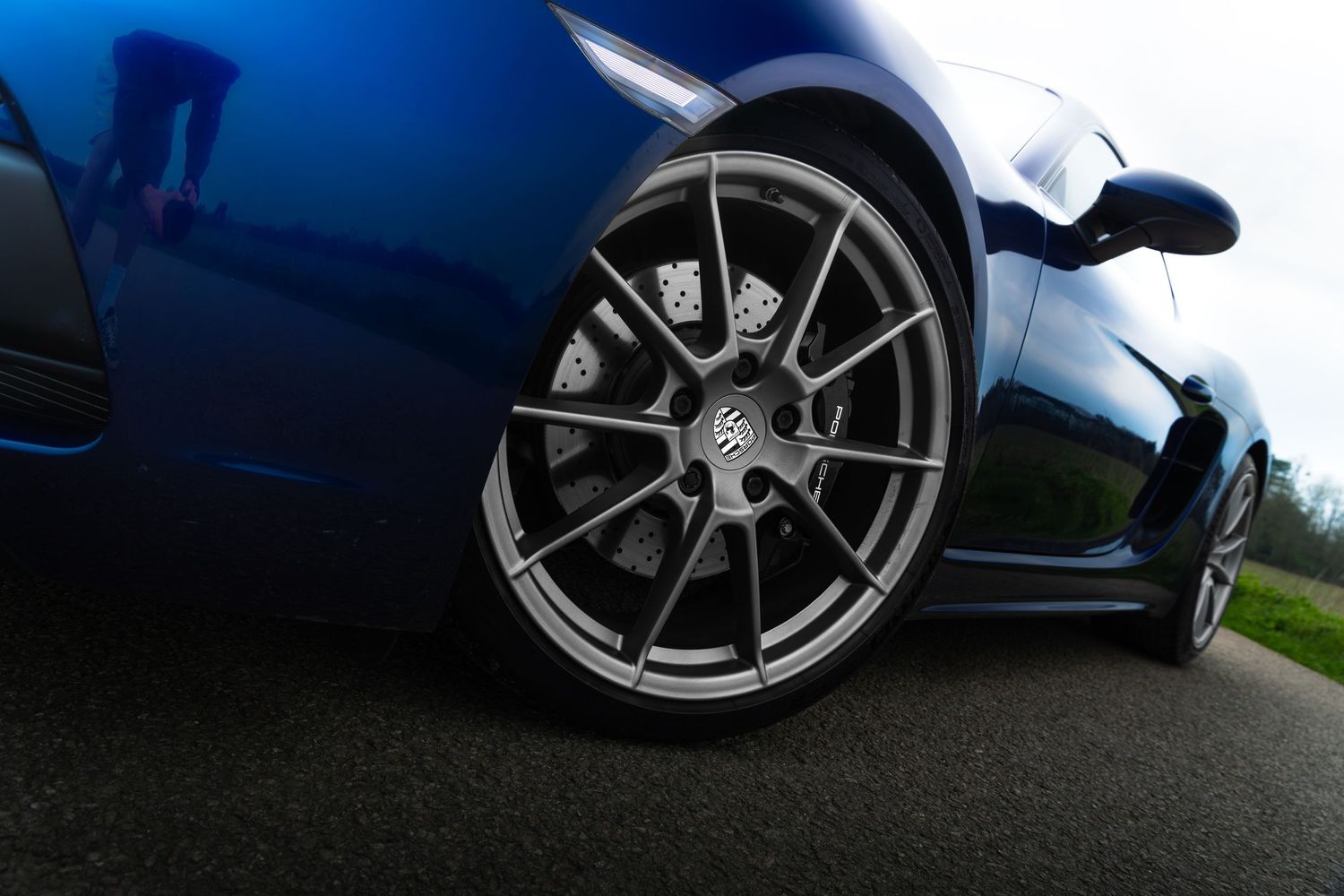 Close-up of Porsche 718 Cayman grey alloy wheel with brake caliper on blue sports car.