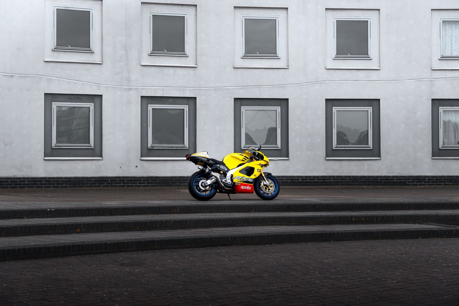 Yellow Aprilia RSV sport motorcycle parked in front of a grey building exterior.