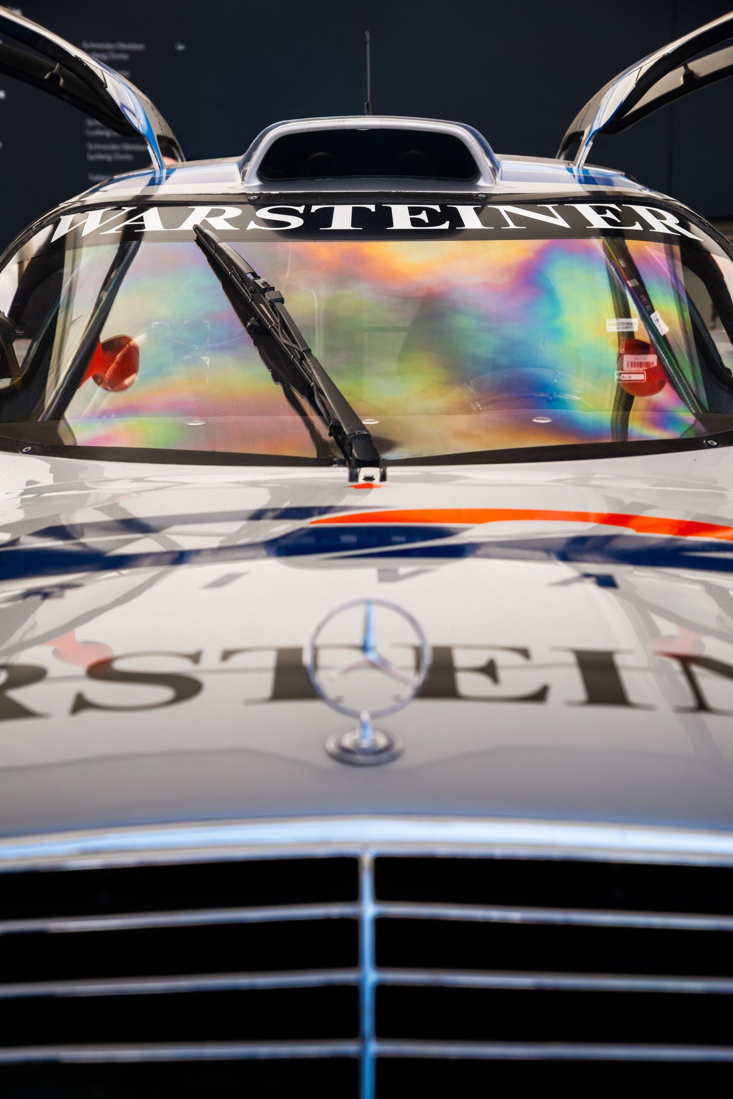Front view of a Mercedes-Benz Warsteiner racing car with iridescent windshield reflections and gull-wing doors open.