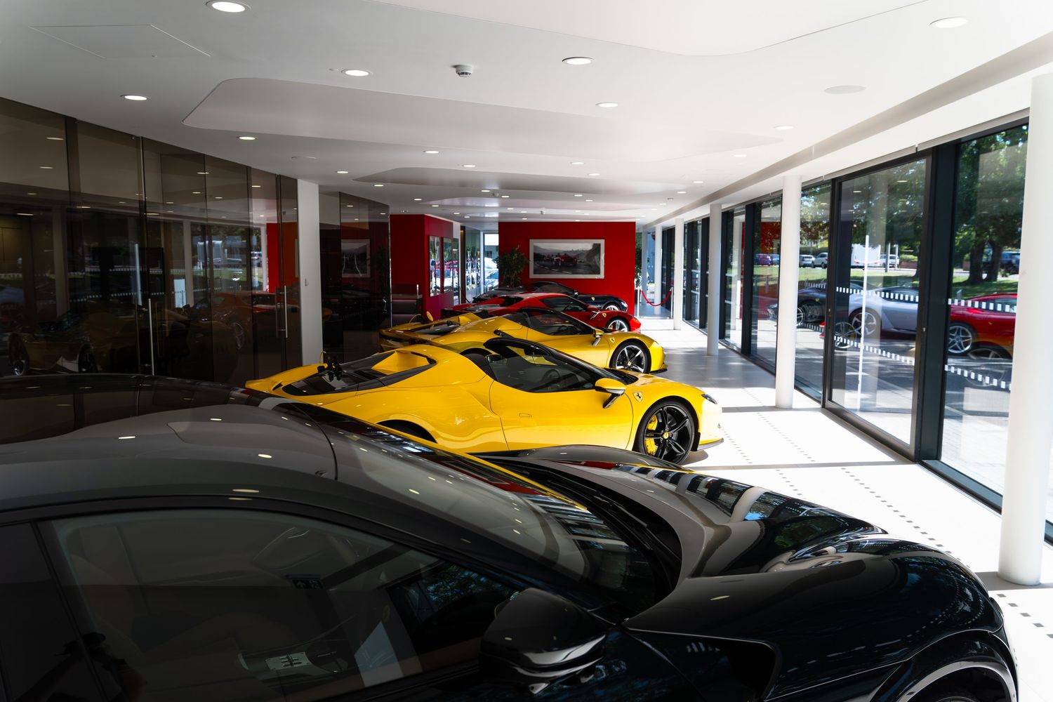 Luxury Ferrari dealership showroom featuring yellow and black sports cars displayed on a polished floor with floor-to-ceiling windows.