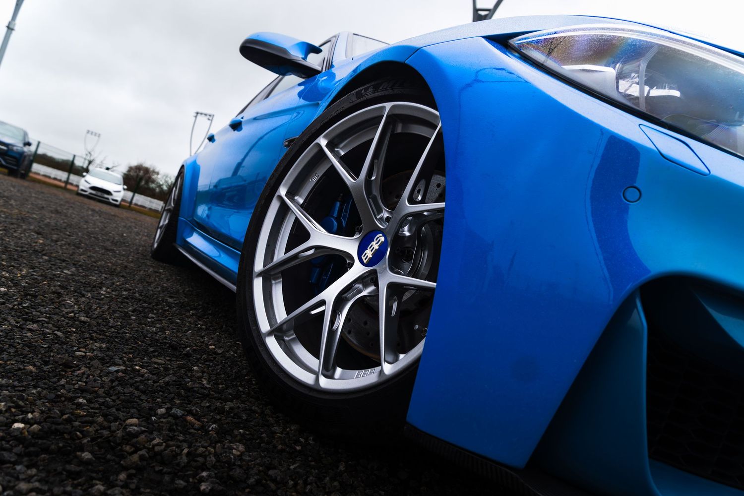 Low-angle shot of a blue sports car's alloy wheel and wide body kit.