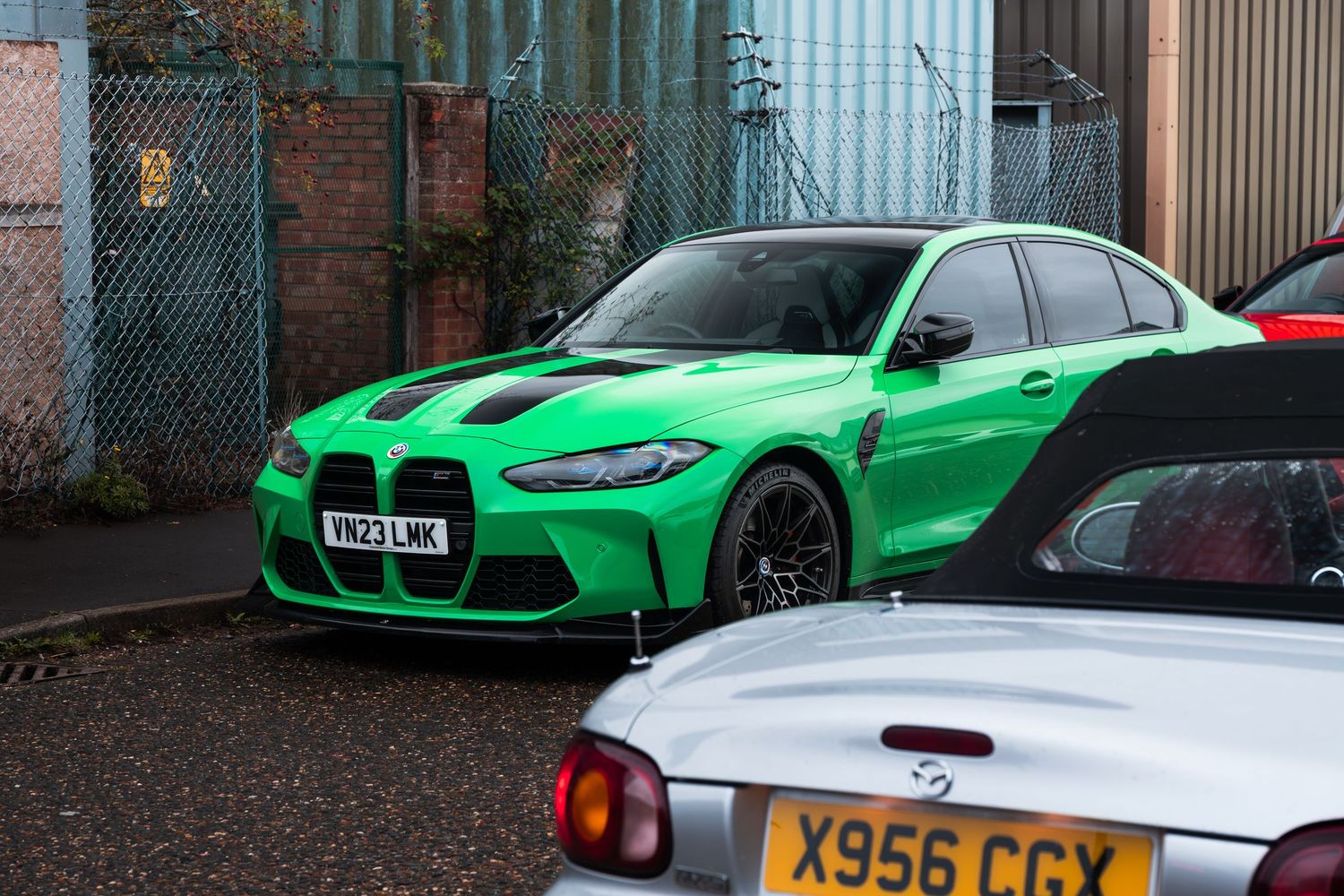 A vibrant green BMW M3 with wide body kit parked at a car meet near industrial buildings.