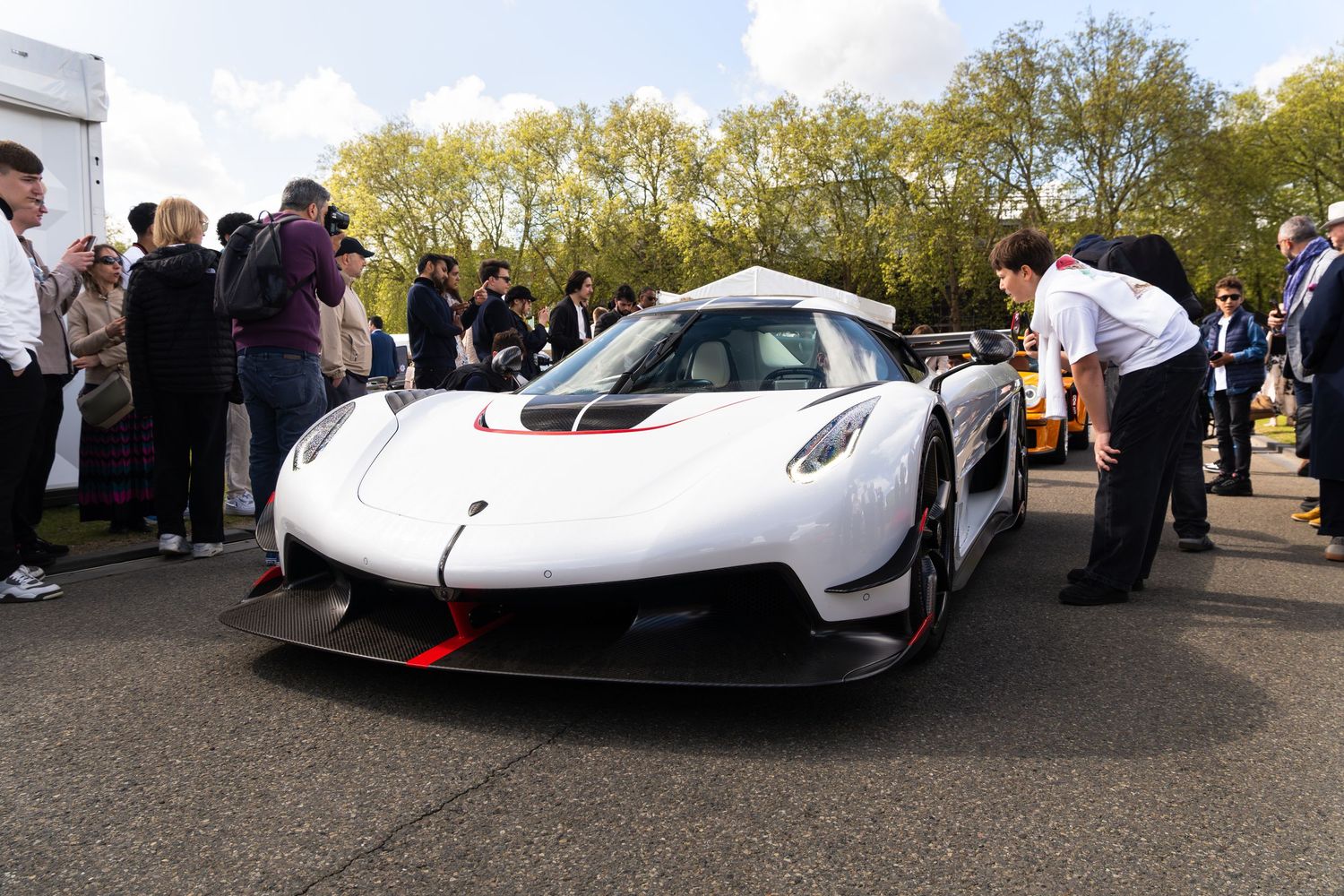 White Koenigsegg Jesko hypercar with red accents surrounded by spectators at outdoor car show.