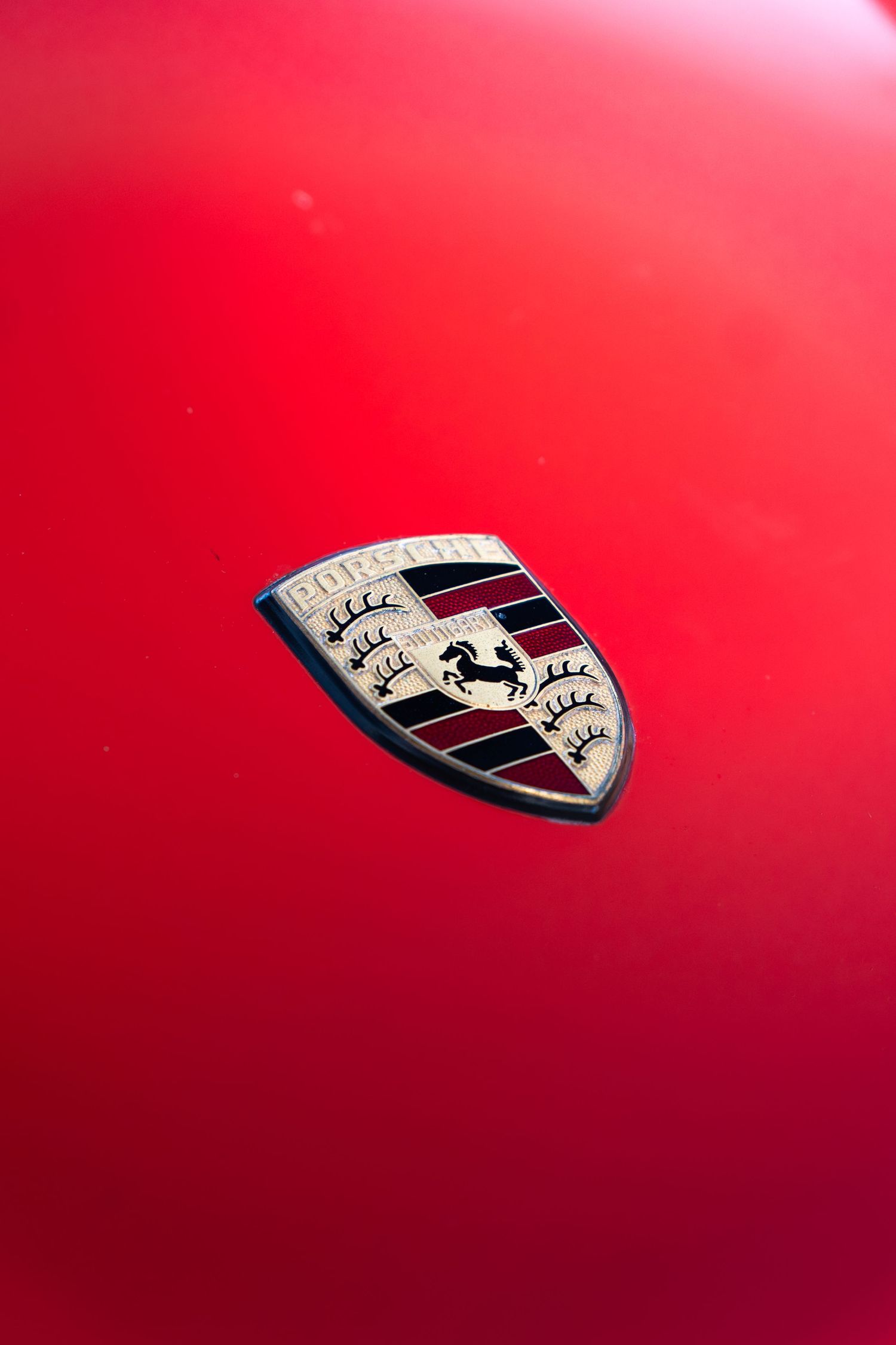 Close-up of the Porsche crest badge on a vibrant red hood of a classic Porsche 911 sports car.