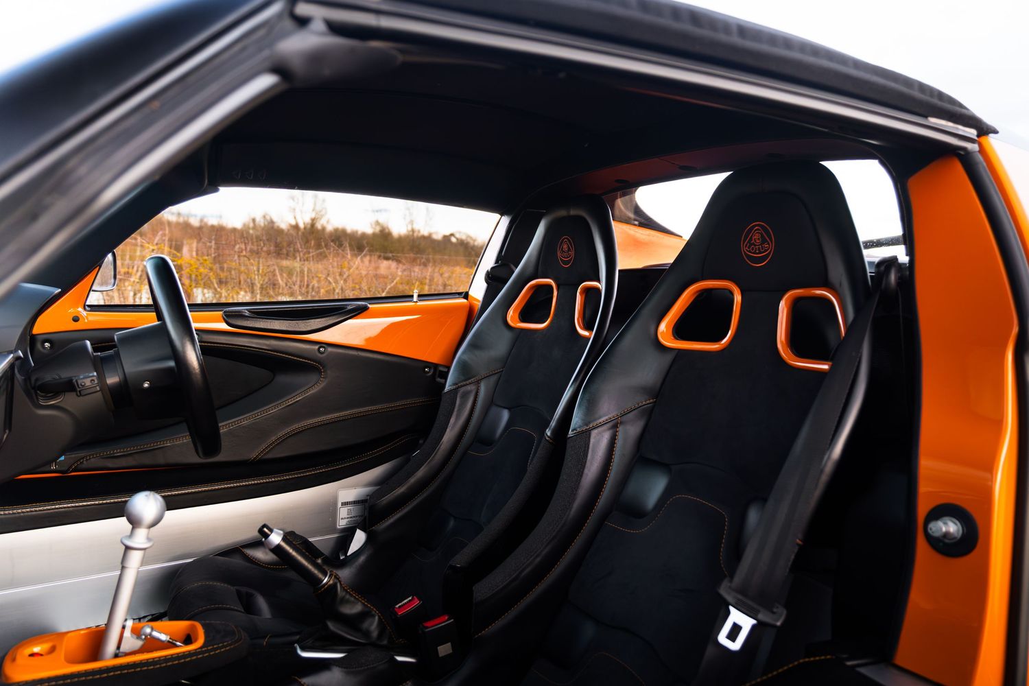 Lotus Elise interior showing black and orange bucket seats and dashboard.