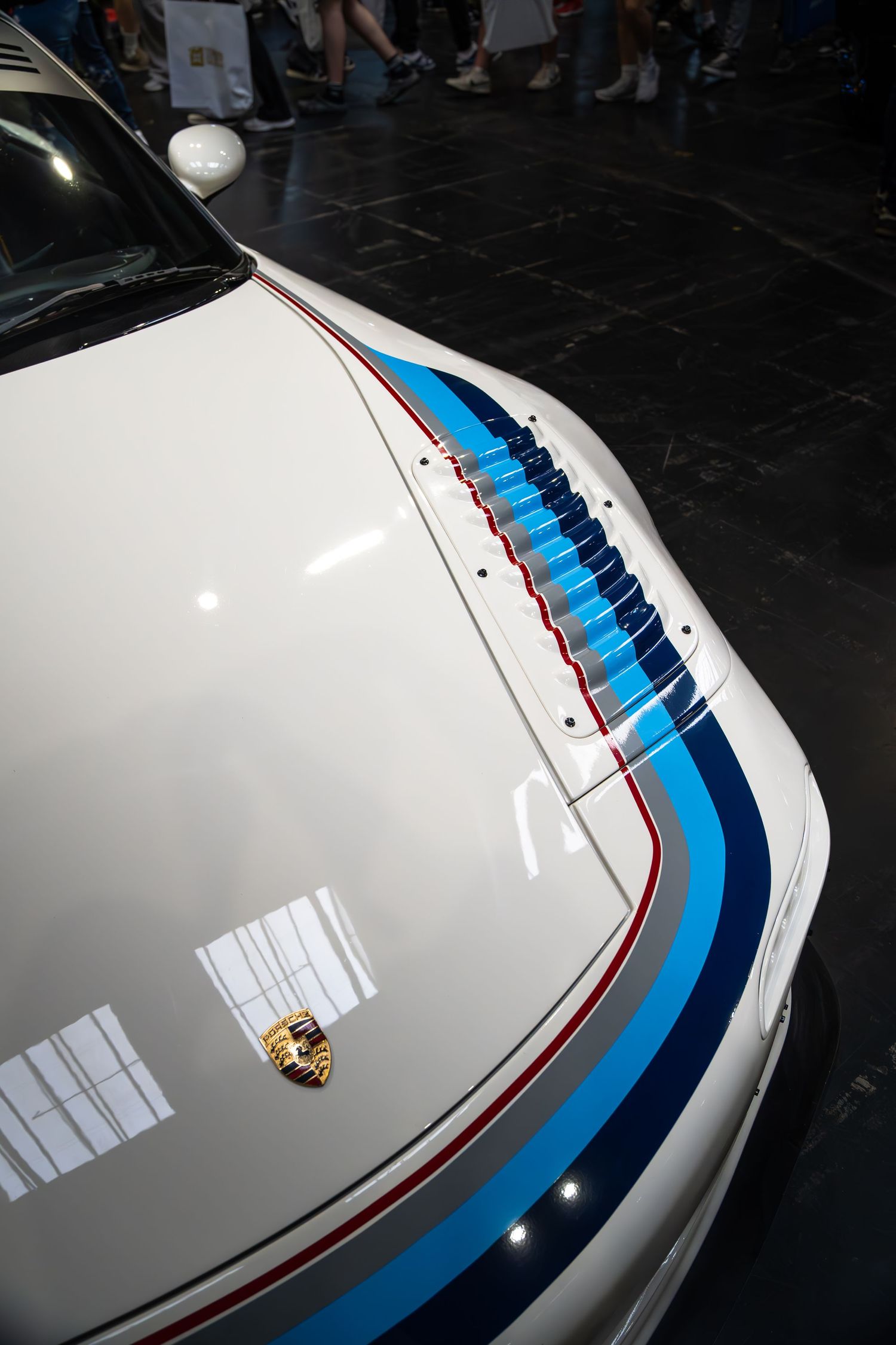 White Porsche race car hood with blue Martini racing stripes at automotive show.