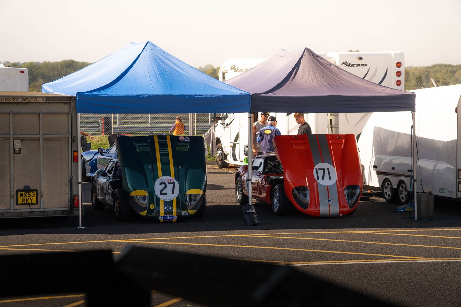 Two racing cars numbered 27 and 71 parked under colorful canopy tents in pit area.