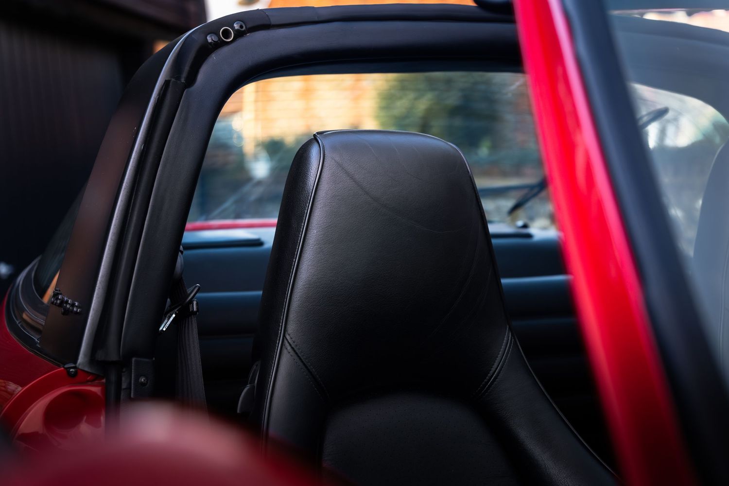 Black leather headrest detail of a Porsche 911 Carrera interior with red door frame and open soft top.