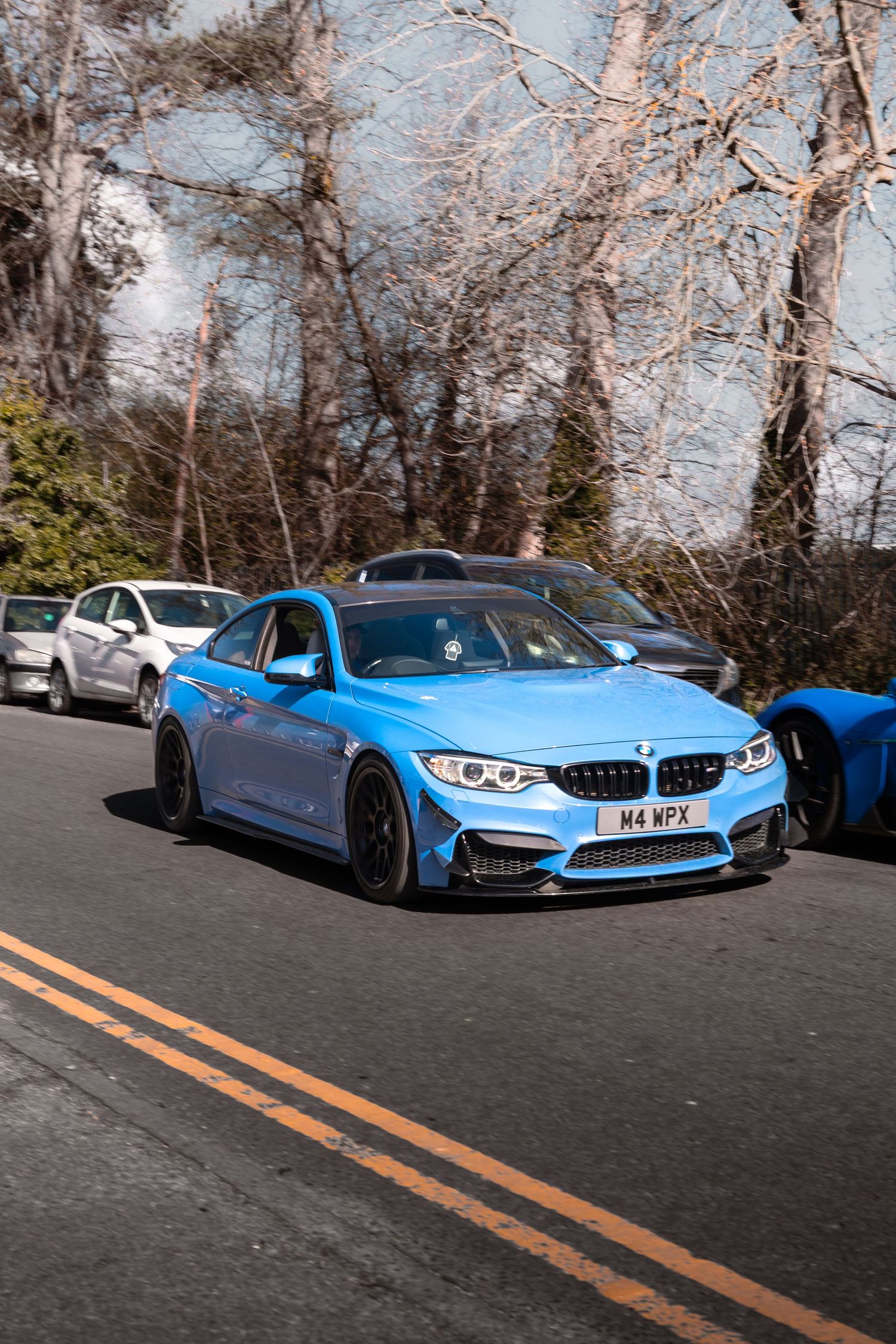 Yas Marina blue BMW M4 with carbon splitter on a tree-lined road.