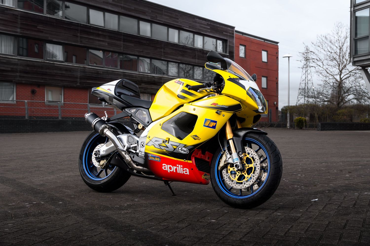Yellow Aprilia RSV sportbike photographed from the front-side angle in an urban parking area.