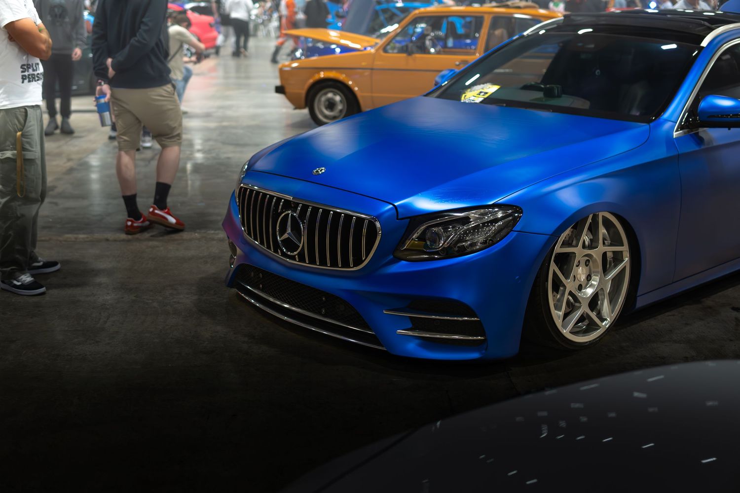 Matte blue Mercedes-Benz sedan with chrome wheels on display at a custom car show.