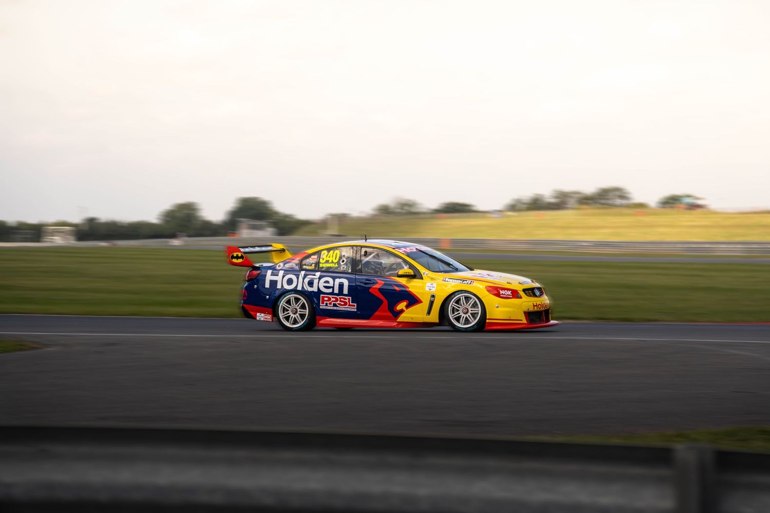 Holden Supercars racing vehicle speeding on track at sunset.