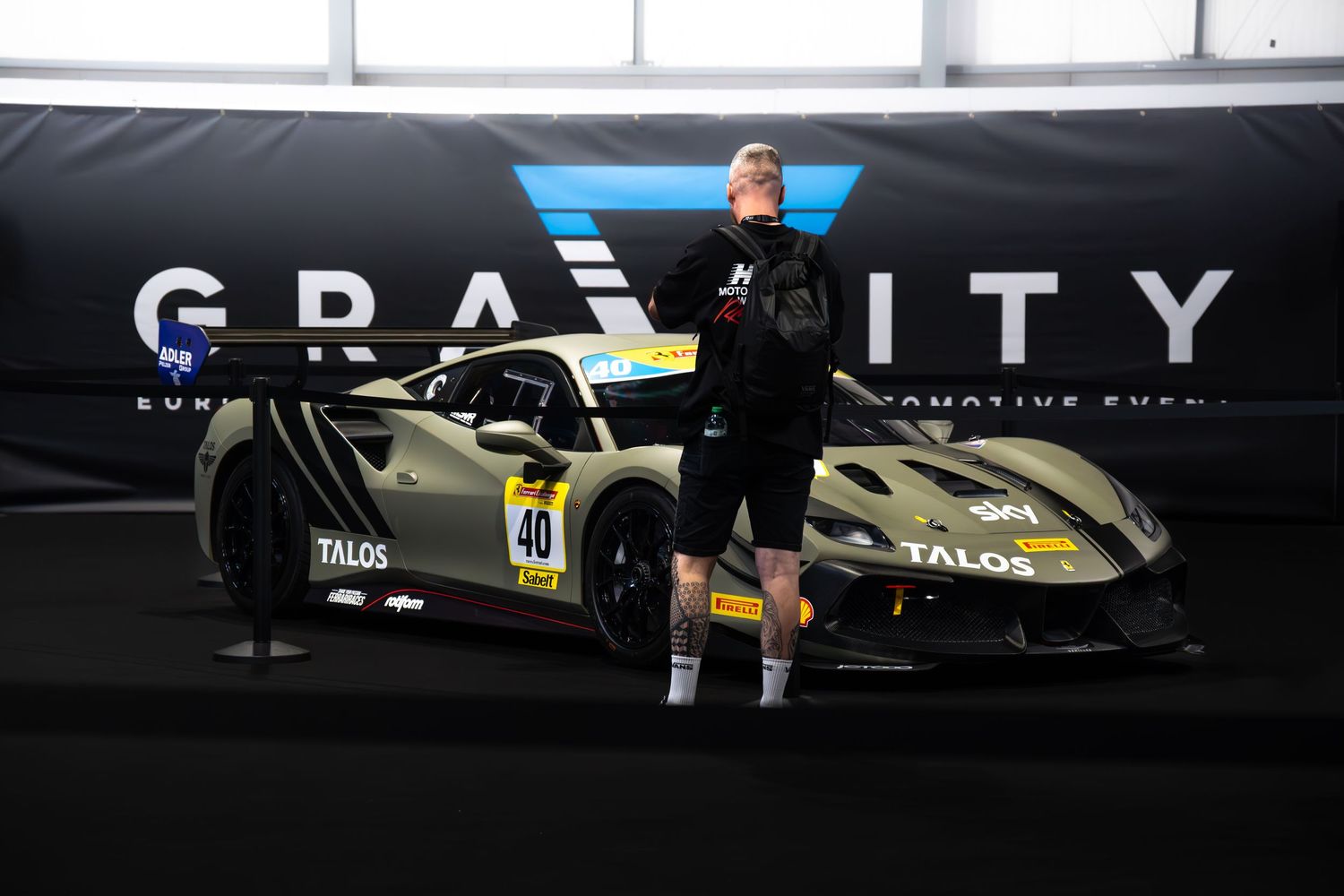 Man posing beside a matte gold Lamborghini Huracan GT race car with number 40 at Gravity event.
